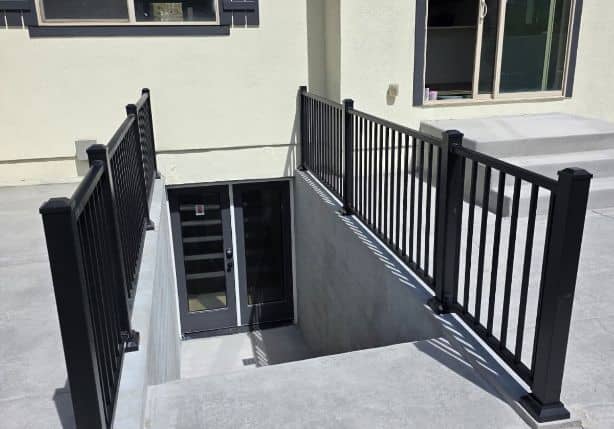 Concrete walkout basement stairwell with black metal railings and the basement door at the bottom