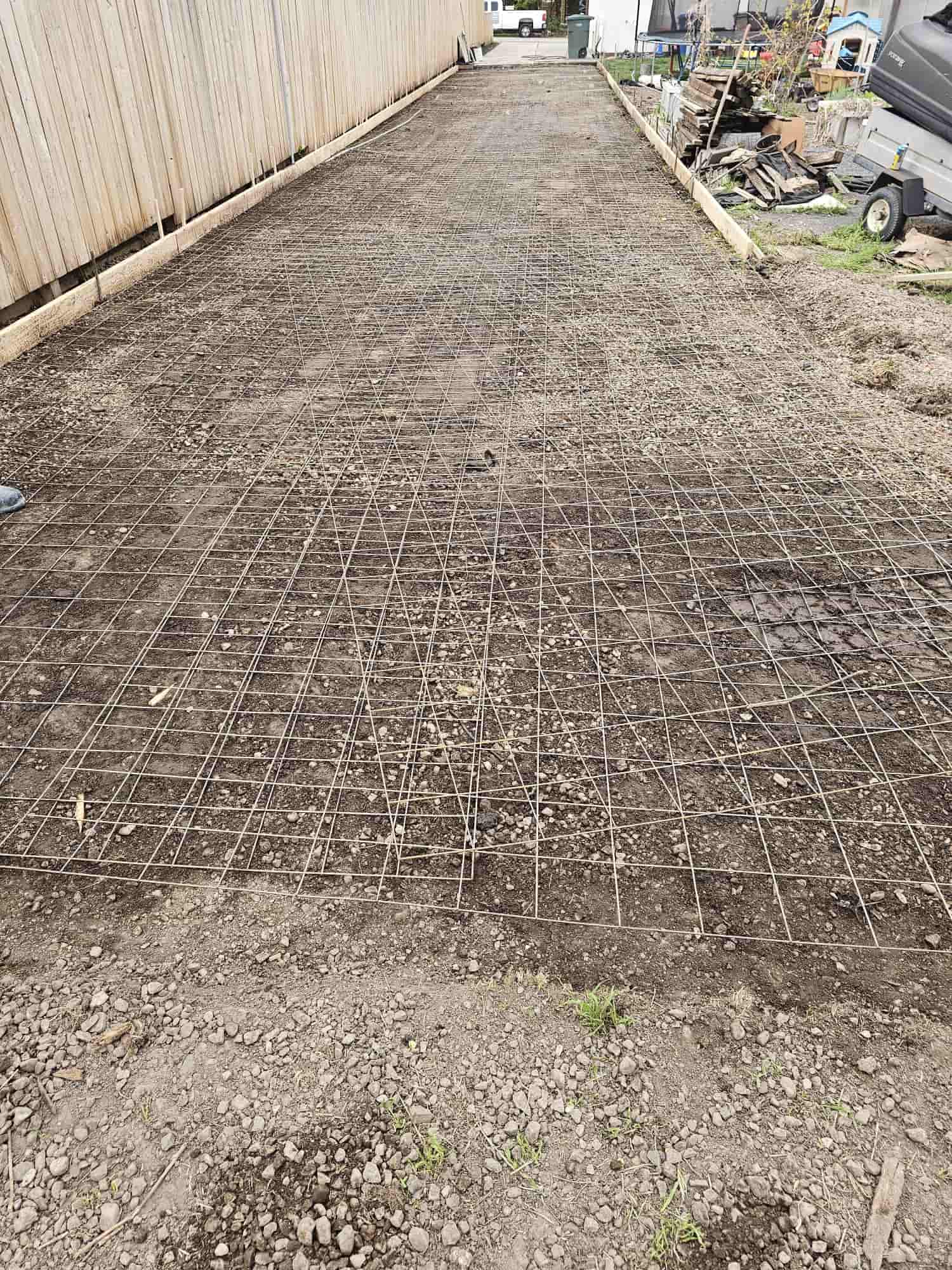 Reinforcing mesh laid across a compacted driveway subgrade between a fence and a house, ready for concrete