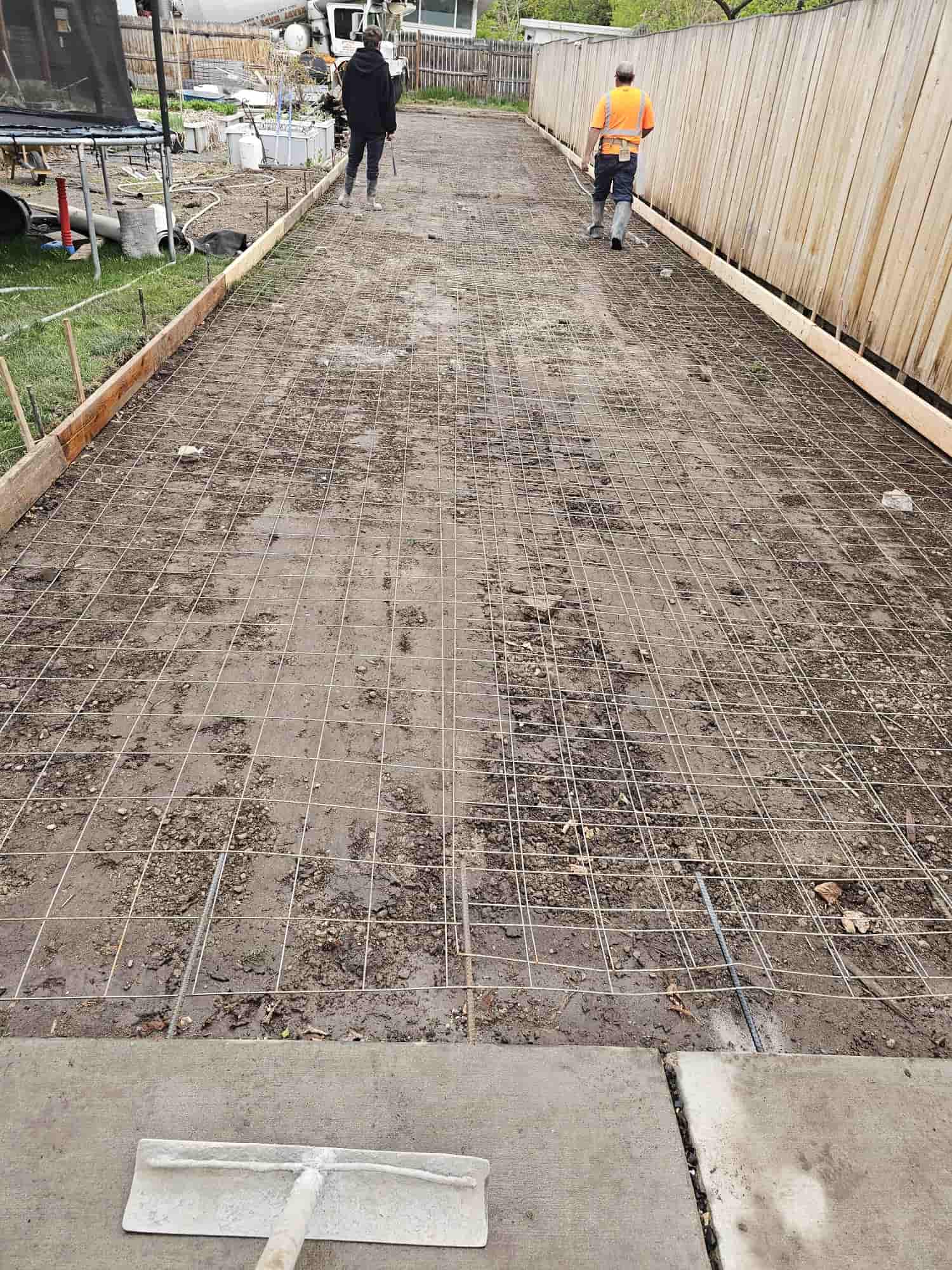 Two crew members walking a formed driveway with reinforcing mesh in place as the mixer truck backs in