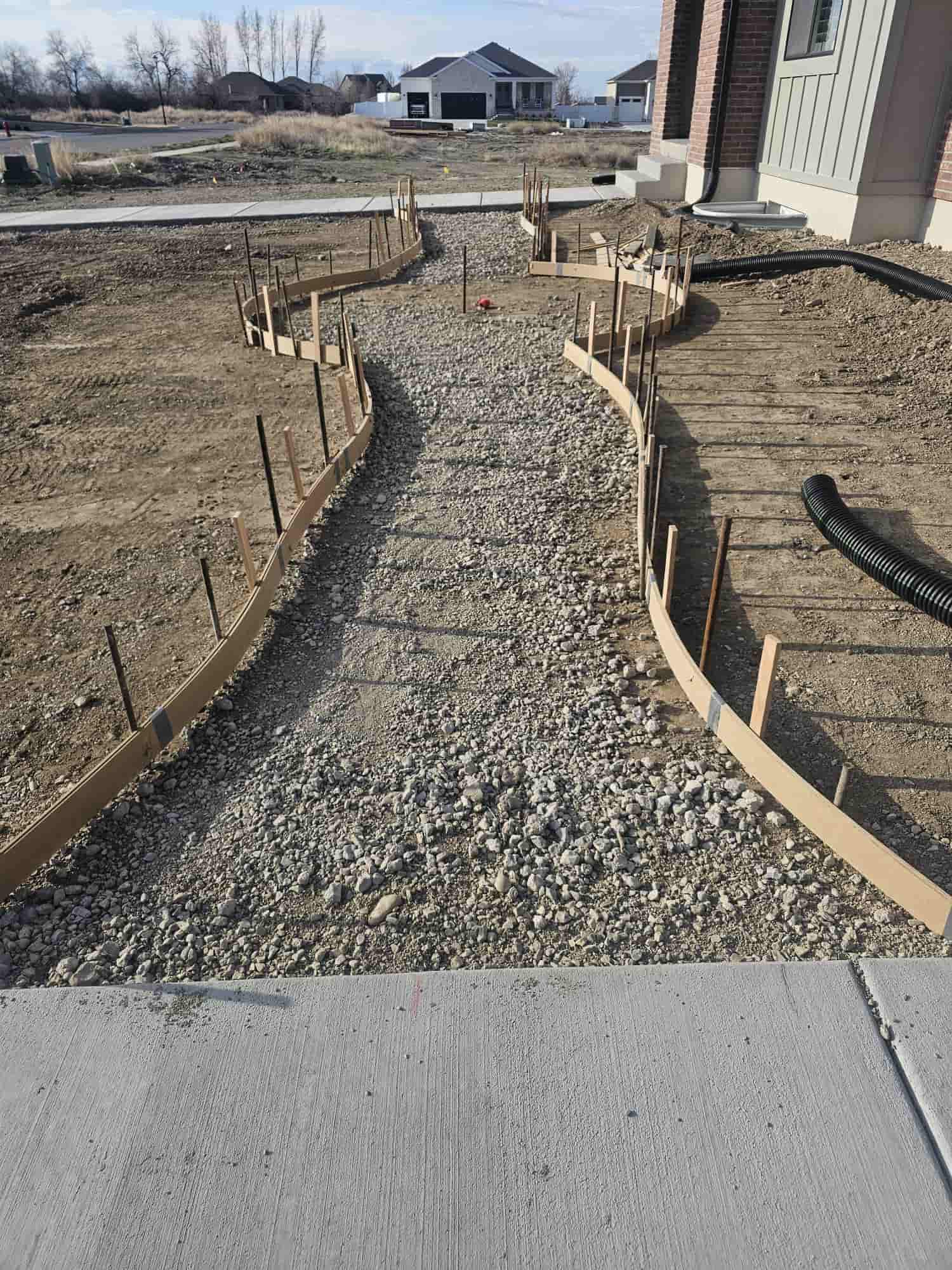 A curved walkway formed in flexible board and staked with rebar, running from the driveway to a new home