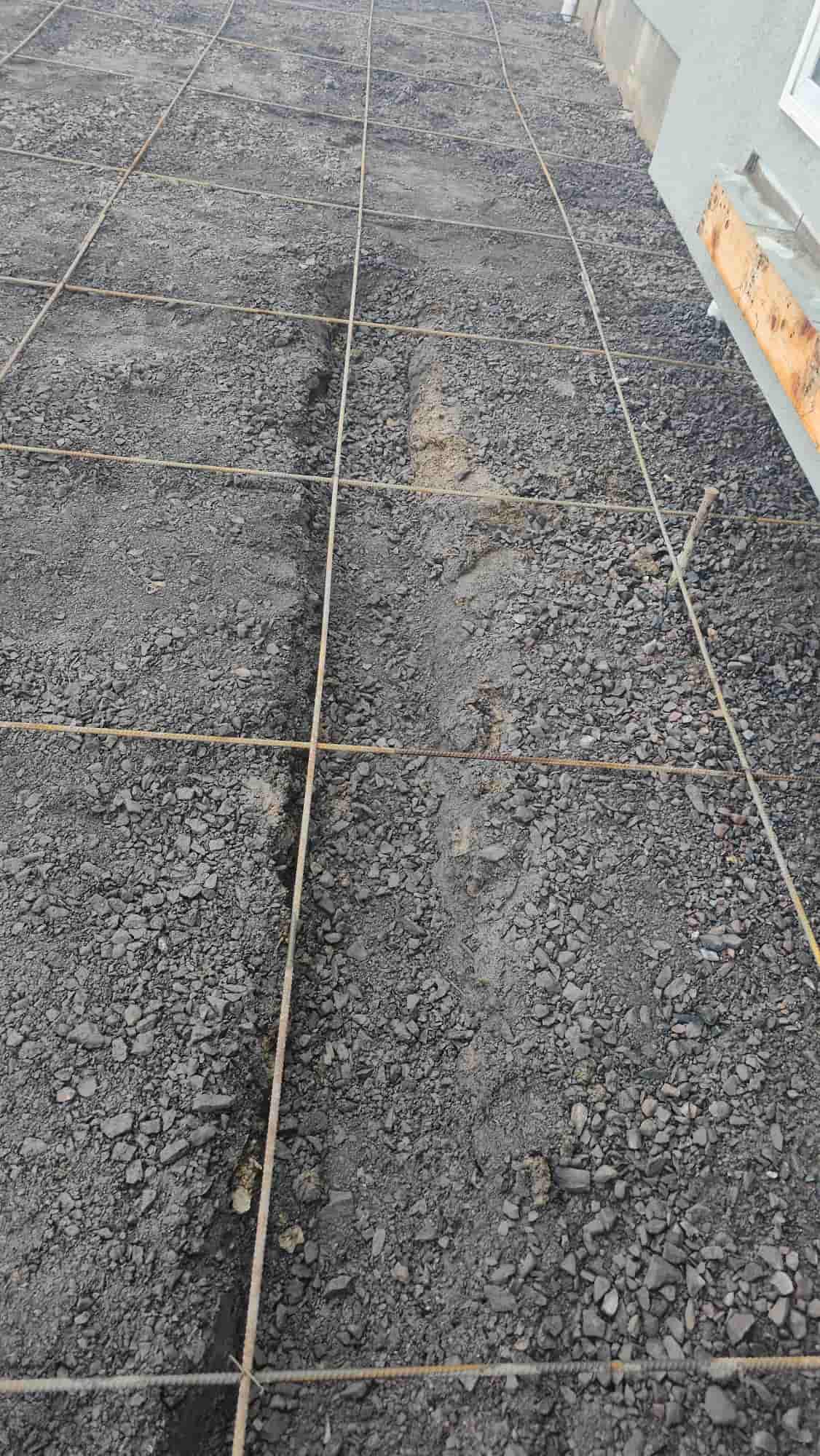 Rebar grid tied over a gravel subgrade against a foundation wall, prepared for a slab pour