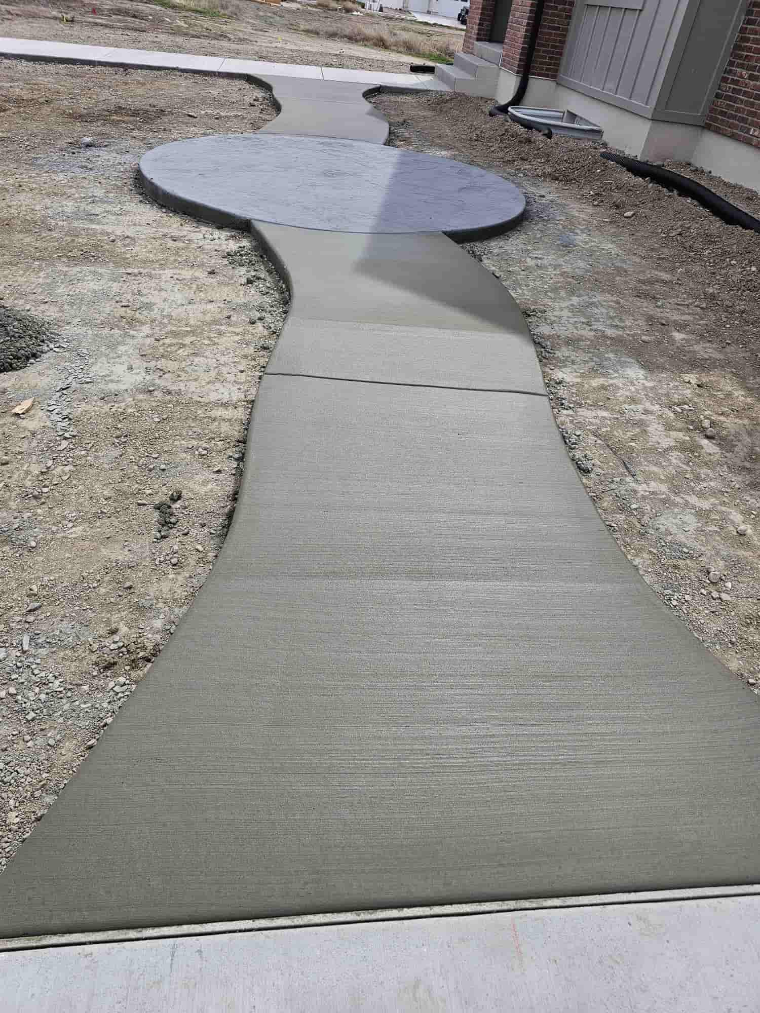 A finished broom-textured concrete walkway curving away from a house, with control joints cut across it