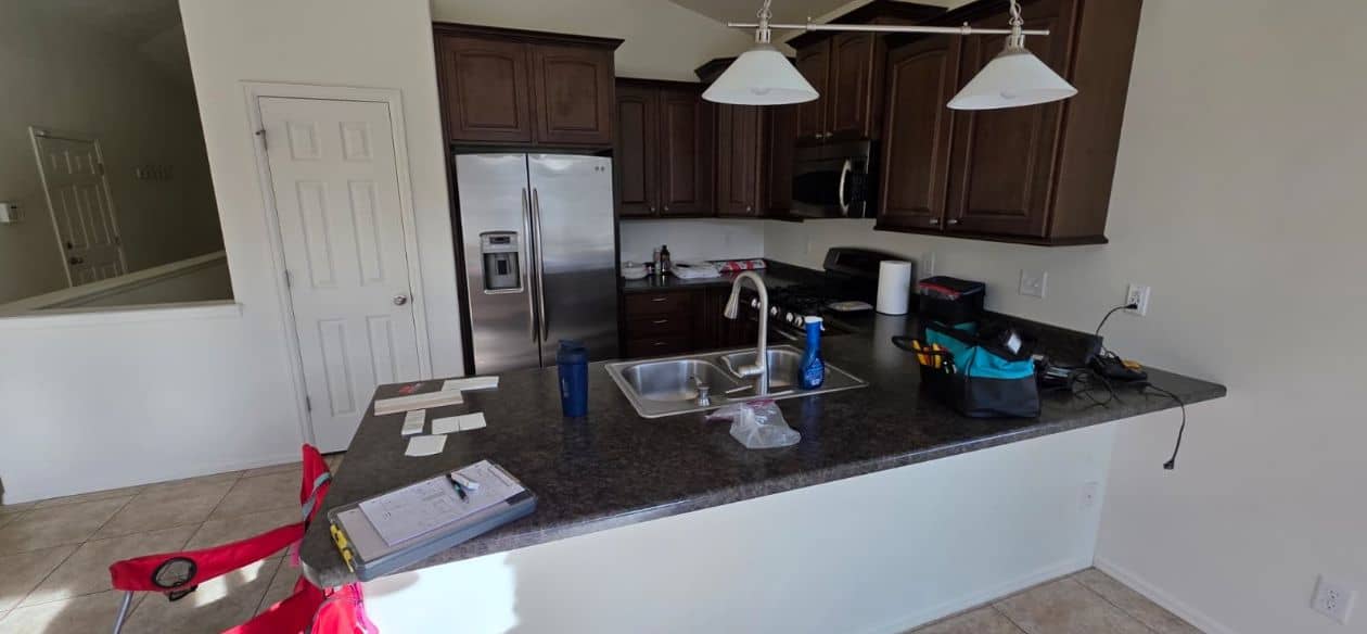 Kitchen mid-remodel with dark wood cabinets, a granite peninsula sink and a stainless refrigerator