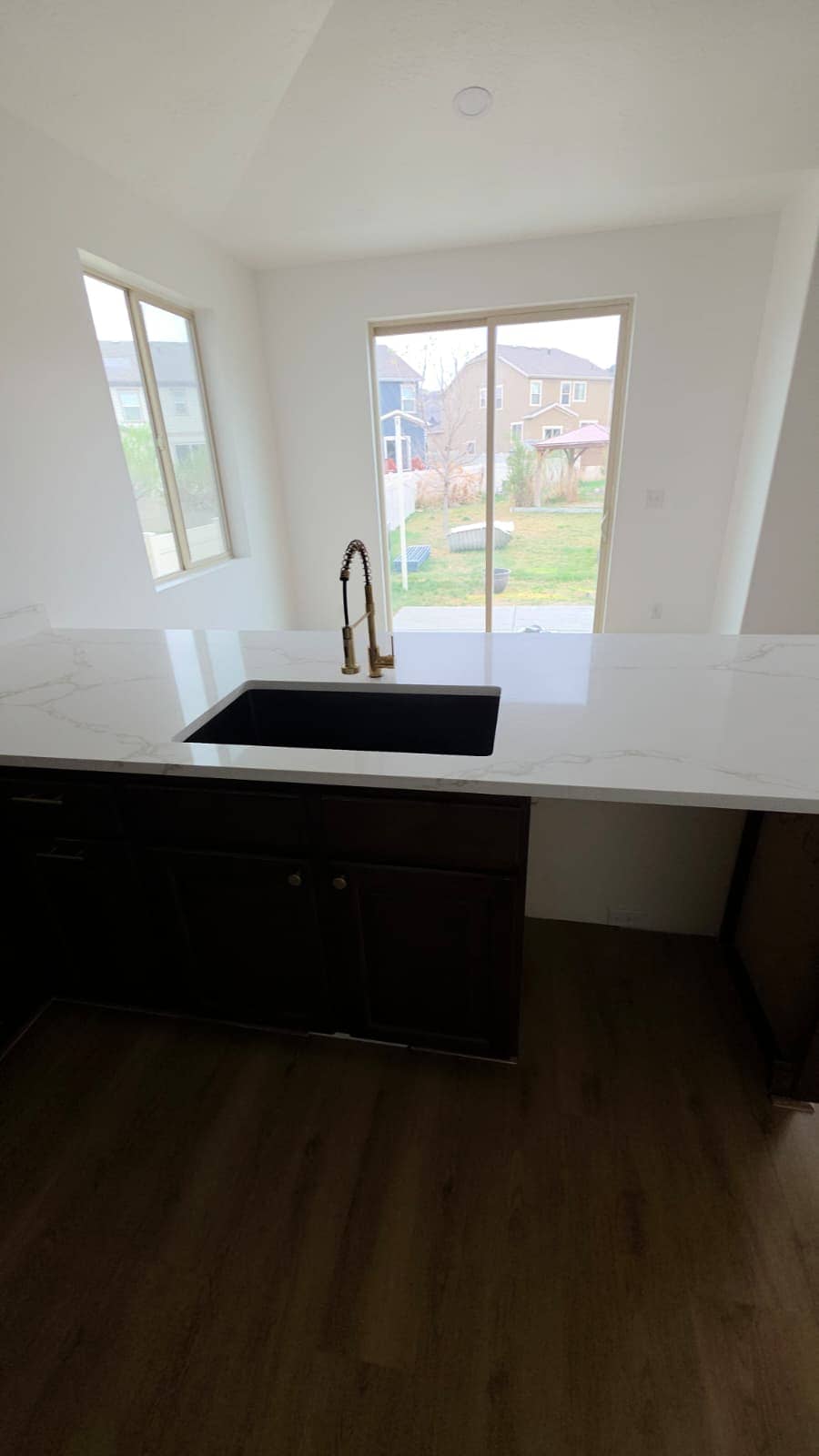 Kitchen island with a white quartz top, black undermount sink and gold faucet over dark cabinets