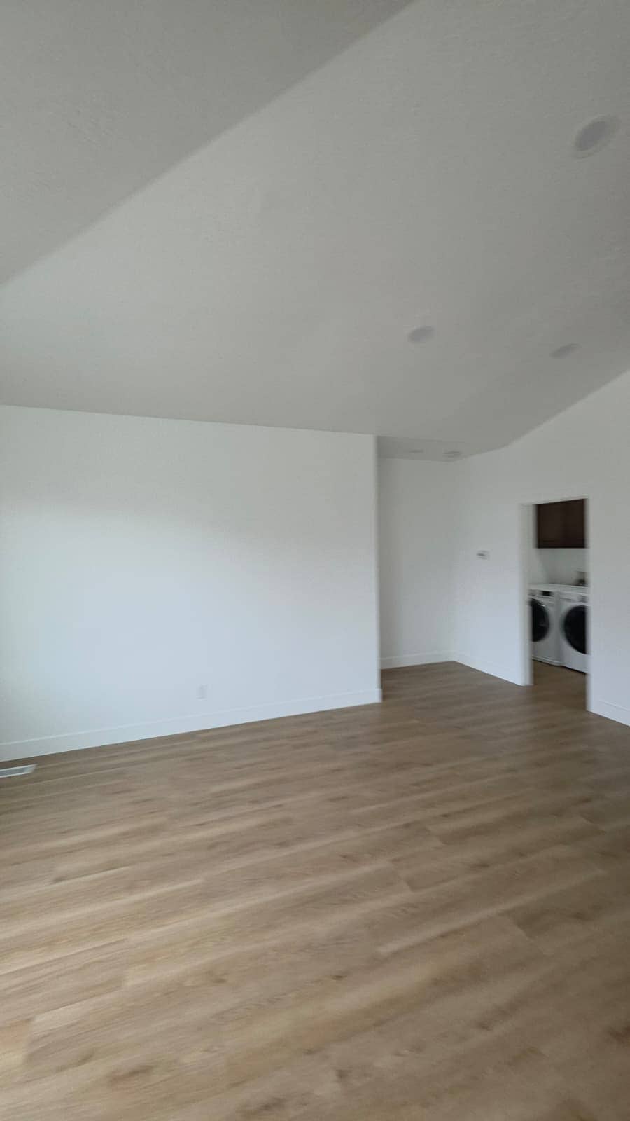 Finished room with freshly painted white walls, a vaulted ceiling and vinyl plank flooring