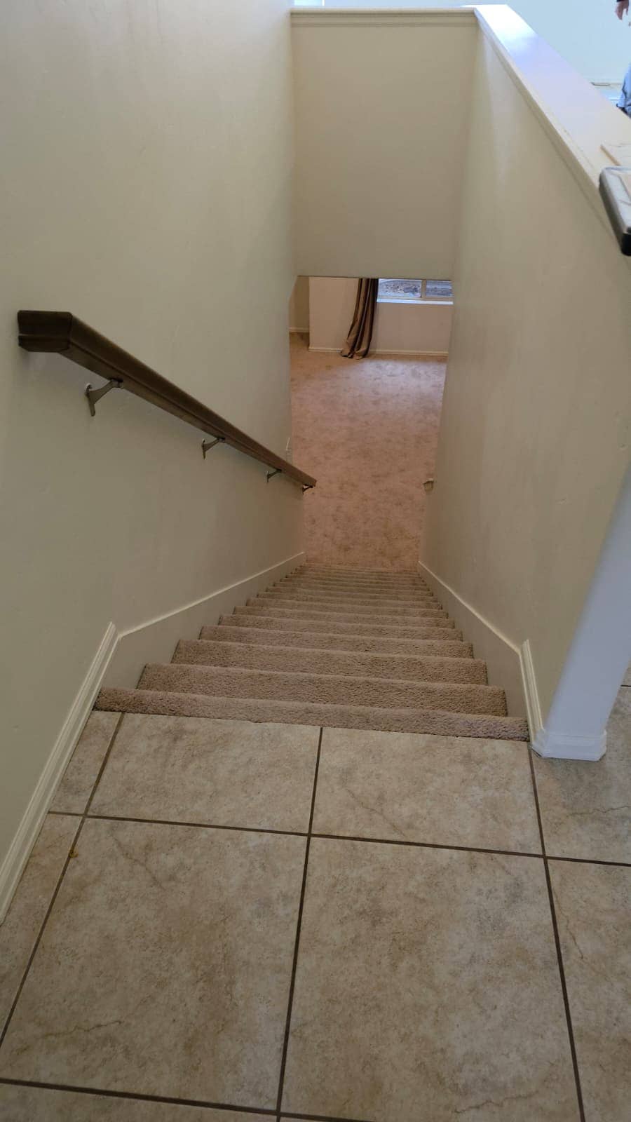 Carpeted stairs leading down from a tiled landing with a wood handrail
