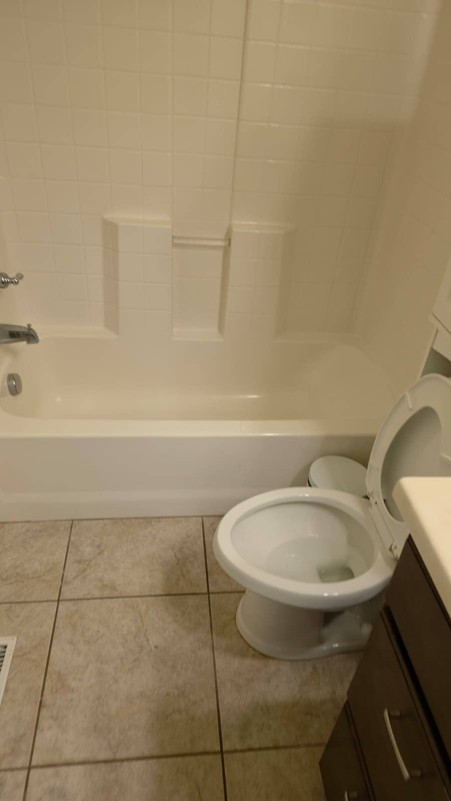 Bathroom before its remodel, with a tub and tile surround and a beige tile floor