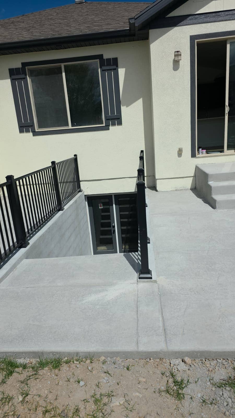 Basement entry stairwell with railings and new concrete flatwork beside a stucco house
