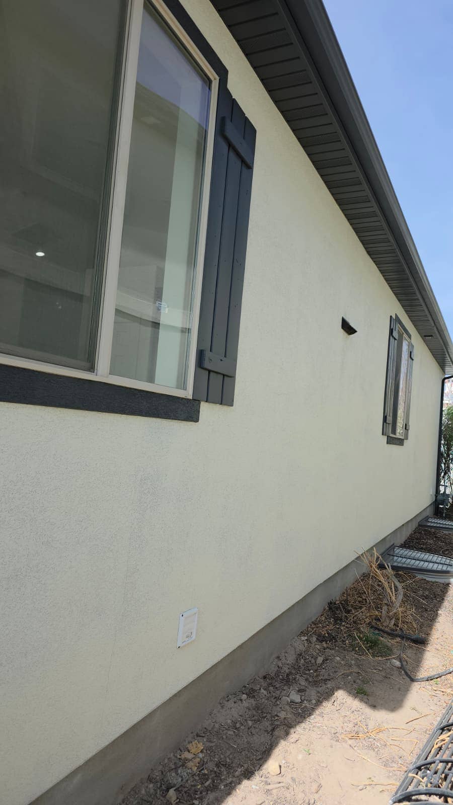 Long stucco side wall of a house with dark shutters and windows