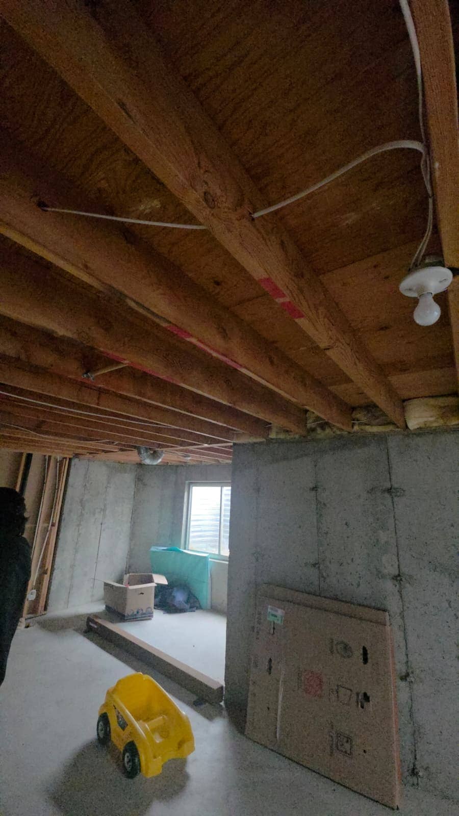 Unfinished basement before the remodel, with exposed joists and bare concrete walls