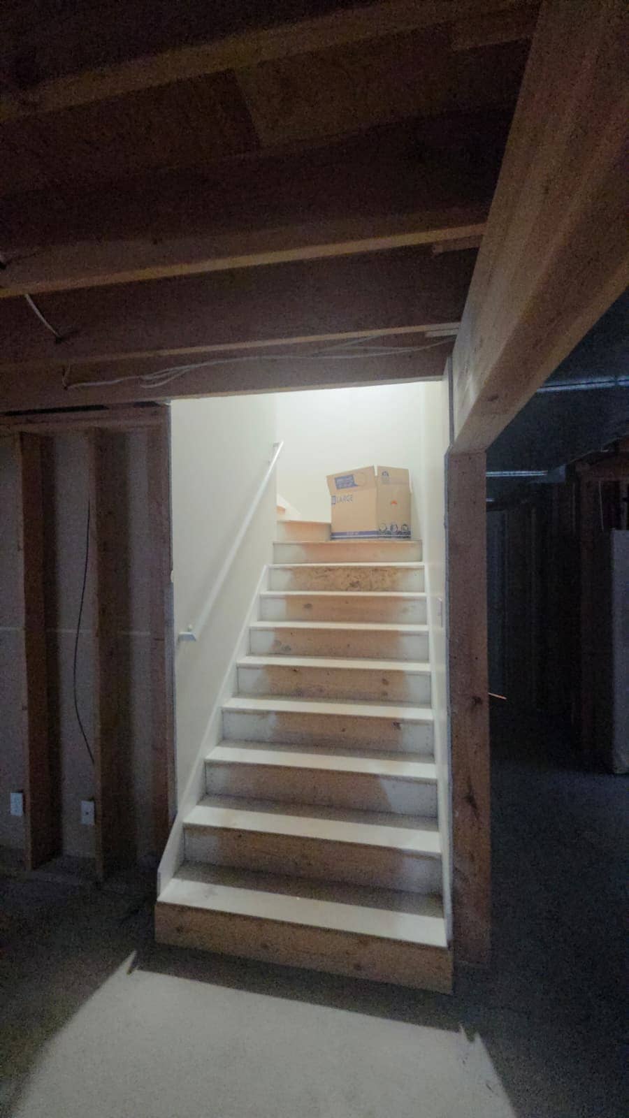 Unfinished basement stairwell with exposed stud framing before drywall