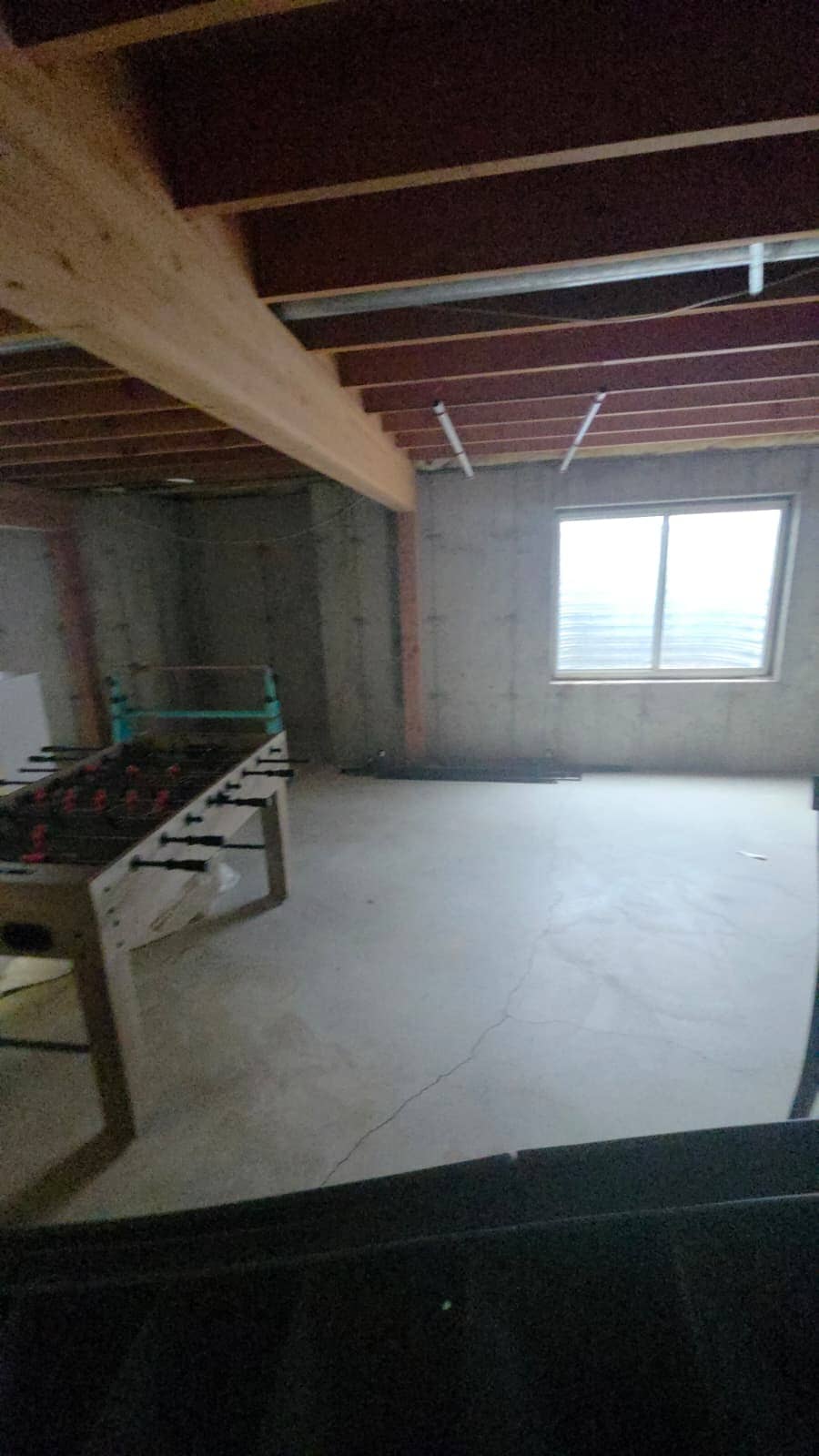 Unfinished basement with bare concrete, exposed joists and a beam, before the remodel